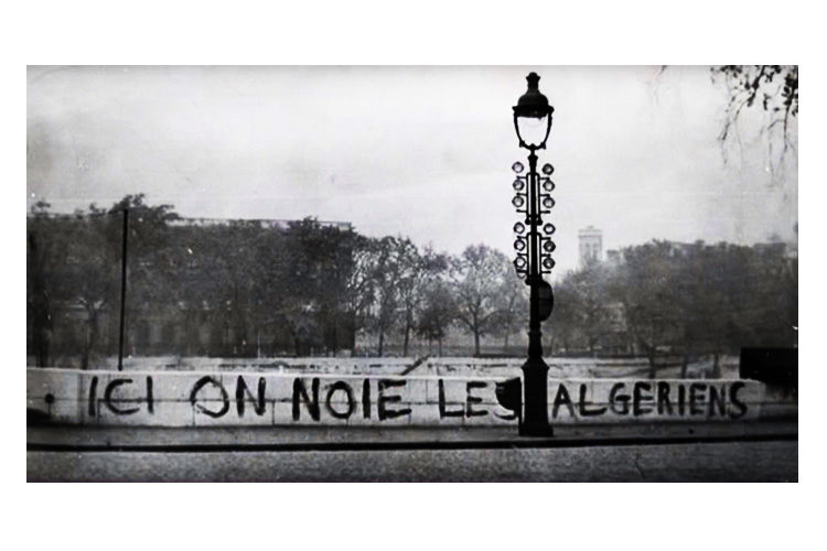 A screenshot from the documentary "Ici on noie les Algériens, 17 octobre 1961" depicting graffiti on a bridge above the Seine River in Paris reading "Here we drowned the Algerians." Several witnesses reported seeing dead bodies floated in the river after the assault by the police. 
